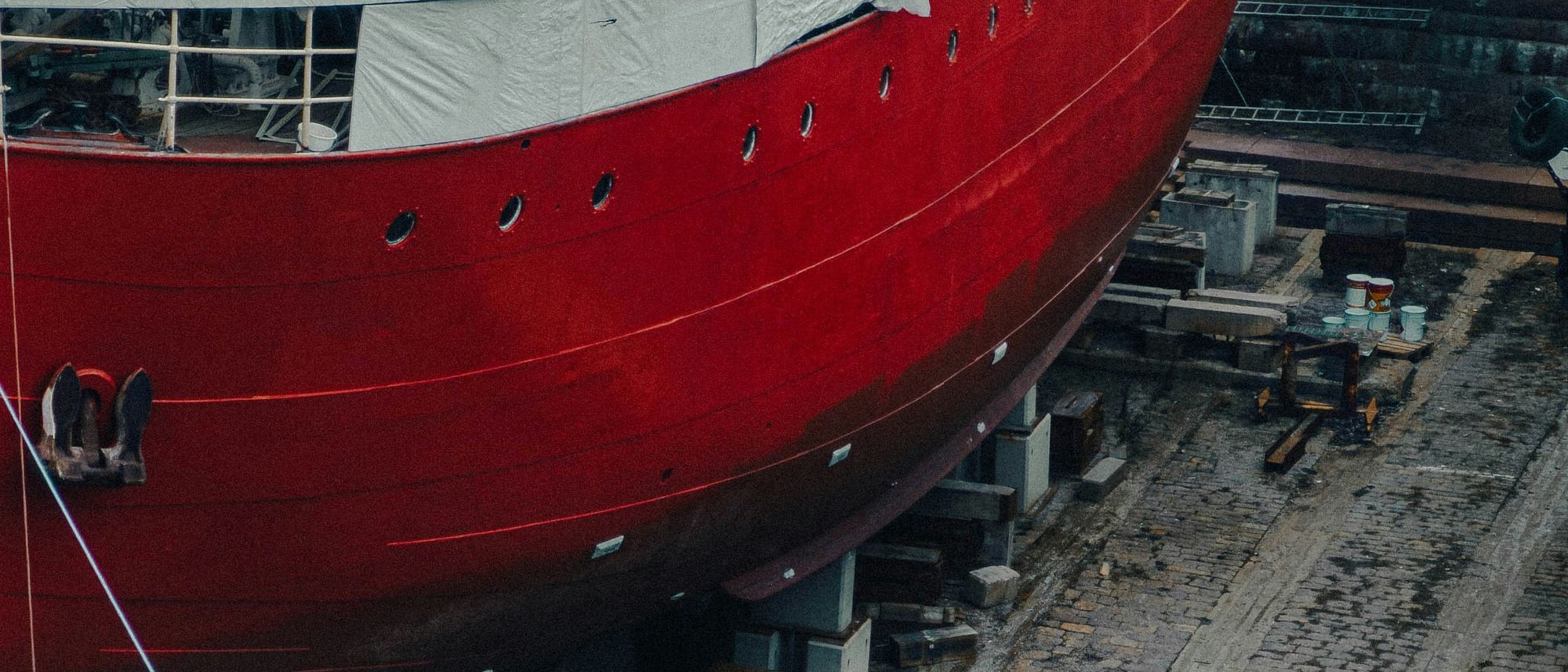 A red-hulled ship under construction in dry dock